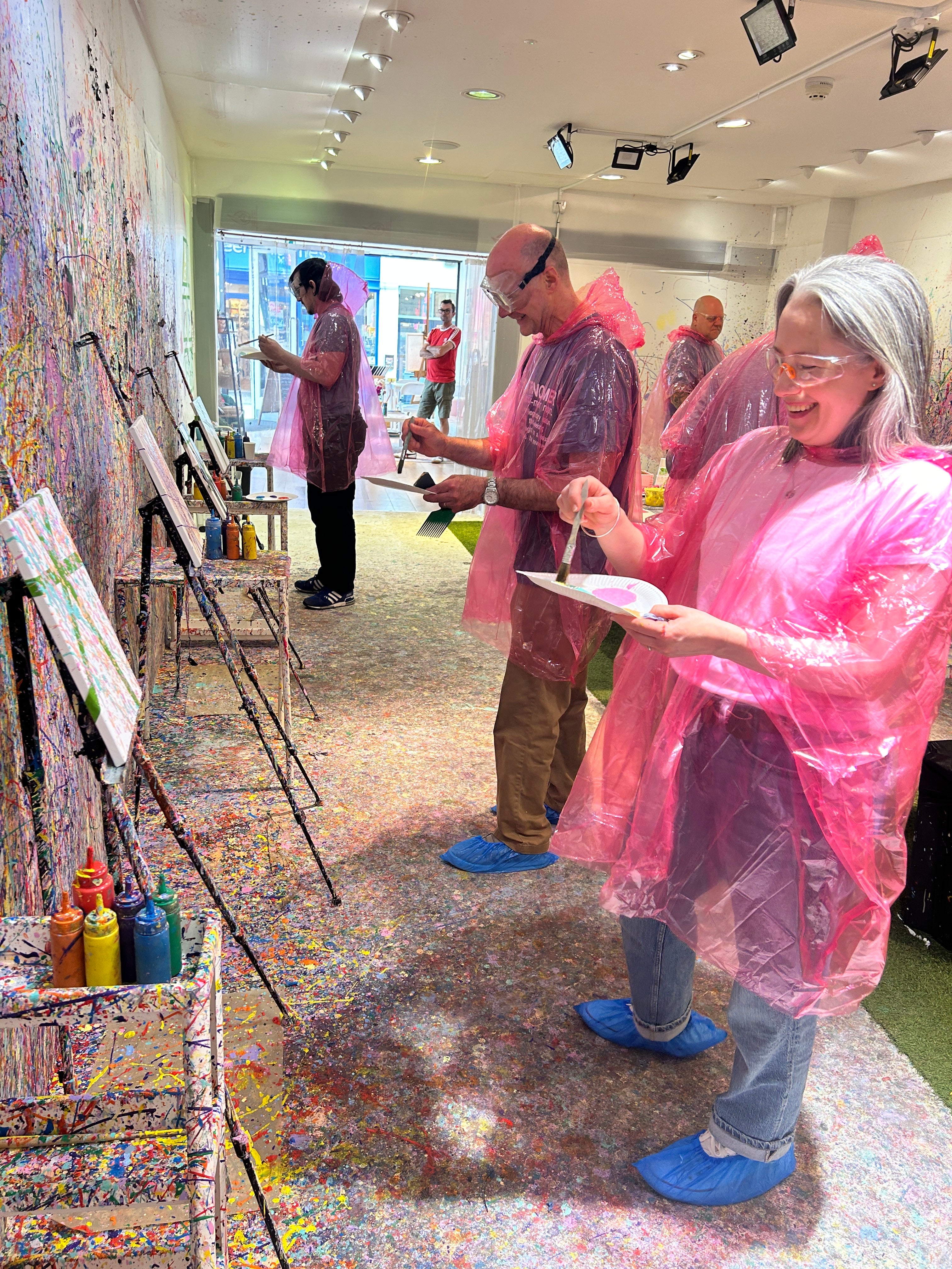 Two people in pink rain ponchos standing in a room with colorful art on the floor.